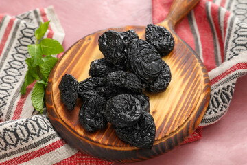 Board with tasty prunes on color background