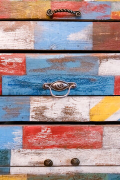 Close-up view of metal cabinet knob on multicolored wooden chest of drawers. Drawers are painted in different colors. Colourful furniture theme.