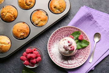 Plate and baking pin with tasty raspberry muffins on dark background