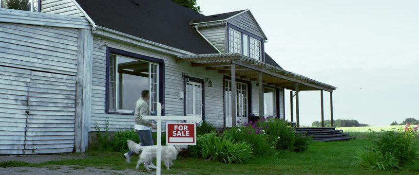 Caucasian couple with a dog passing for sale sign, walking towards an American style house they are planning to buy. Shot with 2x anamorphic lens
