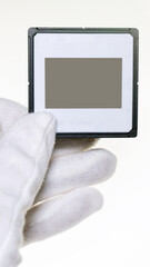 hand with white cotton gloves holding single plastic 35mm slide with empty or blank frame. 9:16...