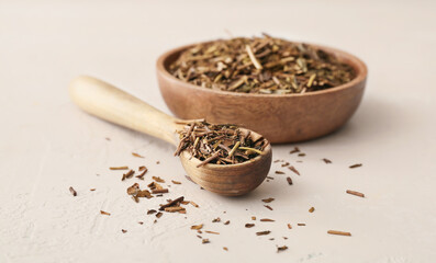 Bowl and spoon with dry hojicha green tea on light background