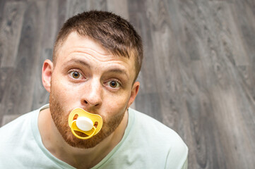 Portrait of a young man with a babys dummy in his mouth. Infantilism concept