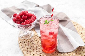 Glass of tasty lemonade and bowl with raspberry on light background
