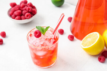 Glass of tasty lemonade and bowl with raspberry on light background