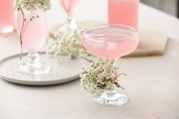 Glasses with tasty cocktail and beautiful gypsophila flowers on light background