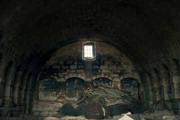 A huge old abandoned barn, made of stone, empty, in the countryside. Darkness all around, light coming from a tiny window on the top.
