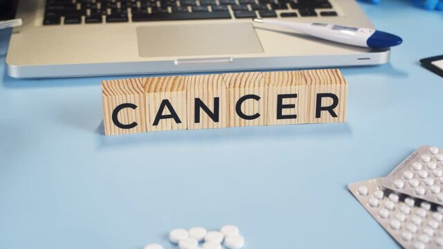 Doctor's gloved hands put cubes with inscription cancer on table. Appearing cubes with word cancer complement medical table full of medicines, closeup