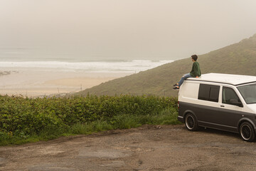 Attractive young female sitting on the roof of a campervan while enjoying the views from the top of a cliff