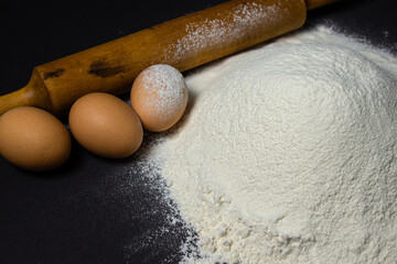 Flour on a black background. Ingredients for dough on a dark surface