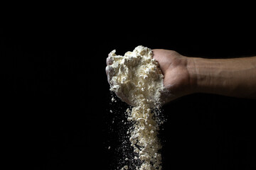 Flour is pouring from the hand on a black background. Flour of the highest grade on a dark...
