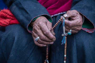 Old Tibetan woman holding buddhist rosary in Hemis monastery, Ladakh, India. Hand and rosary - obrazy, fototapety, plakaty