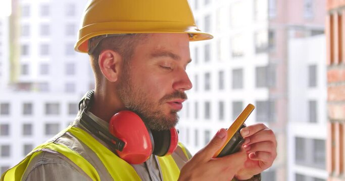 Builder in helmet talking by walkie talkie control and communicate with worker outdoors on construction site at village. Contractor using radio operation in industry. Side view. Close up.