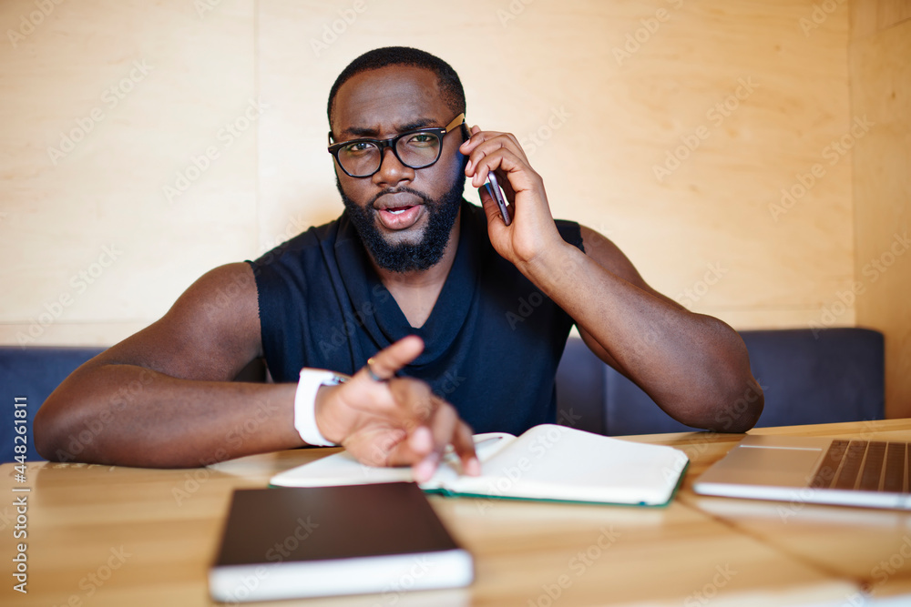 Poster portrait of puzzled male student in optical eyeglasses looking at camera while solving problems duri