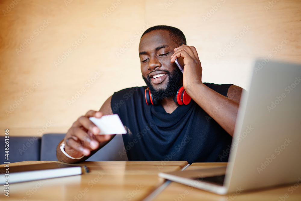 Poster happy dark skinned male programmer with business card smiling while dialing contact number, african 