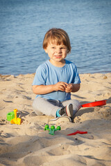 Happy boy sitting on beach and playing with sand. Vacation time concept