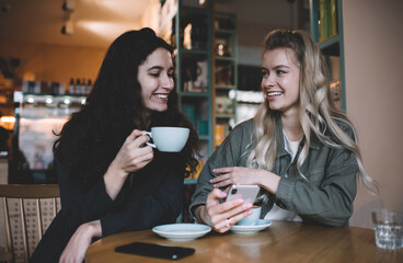 Delighted multiethnic friends with smartphone and cups of coffee