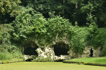 La fausse grotte en rocaille couverte de végétation luxuriante au bout du petit étang au domaine...