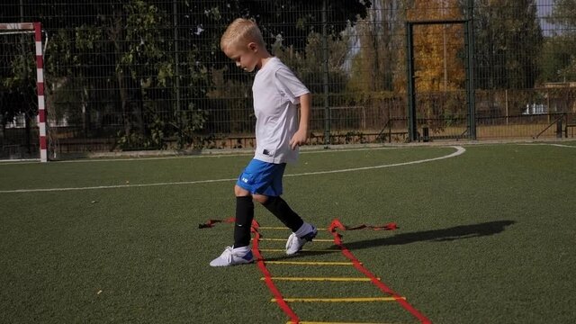 Boy in sportswear improving speed with ladder drills on football field.