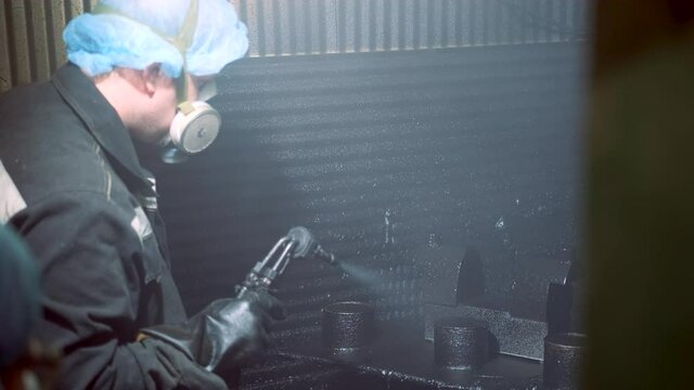 A man in a factory sprays polyurethane on a part. Spraying polyurethane on metal to protect against corrosion and abrasion. Coating with two-component cold curing polyurethanes for industrial products