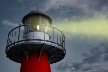 A large white lighthouse shines in the night with a beam of light above the water.