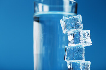 Ice cubes tower with a glass of cold and clean water on a blue background.