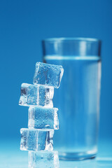 A glass of refreshing water and a tower of ice cubes on a blue background