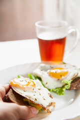 From above anonymous person eating tasty toasts with fried eggs and lettuce for breakfast in morning