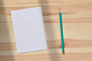 Feuille de papier vierge et crayon posés sur une table en bois brut. Le papier peut accueillir du texte.