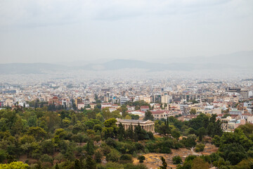 Fototapeta premium View on Temple of Hephaestus in greenery and Athens ancient city center with white buildings on gray foggy day from Areopagus Hill near Acropolis