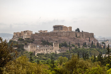 Fototapeta na wymiar Acropolis hill (Parthenon, Propylaea, Temples, Odeon of Herodes Atticus) in summer greenery. Athens ancient historical landmark in city center from Filopappou Hill on cloudy day