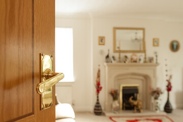 Shallow focus or a gold colour, ornate door handle leading to a large, luxury living room area. A distant fireplace with ornate features is visible.