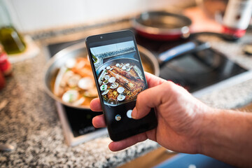 Man takes photos and makes videos of an homemade paella with smartphone at home. Social media...