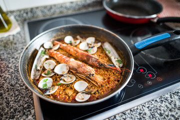 Frying pan on a ceramic hob with freshly made homemade paella at home. Rice with prawns and clams.
