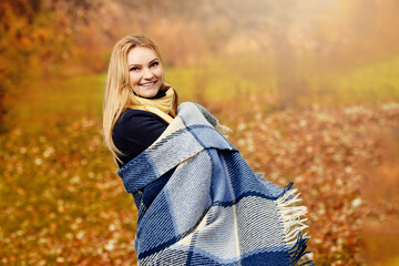 Fototapeta na wymiar Cheerful smiling young blonde wrapped in blanket in autumn forest