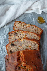 Sweet loaf cake with dried fruit on a baking parchment with a teaspoon of honey and white kitchen towel. 