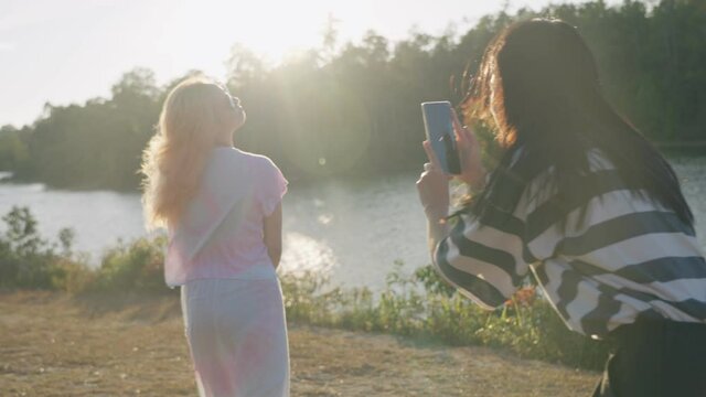 asian girlfriends using smartphone talking pictures for each other and hanging out at outdoor park on sunny day by the natural river stream, posting photo on social media, young lgbt lesbian bisexual