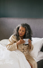 Filipino asian senior woman drinking coffee in bed in the morning