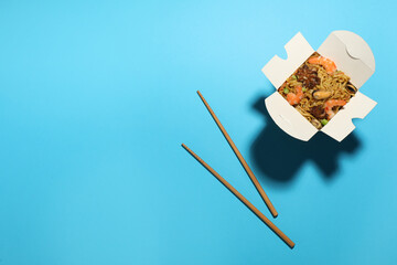 Box of wok noodles with seafood and chopsticks on turquoise background, flat lay. Space for text