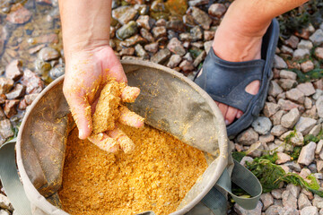 A fisherman's hand is stirring fish bait for fishing in a tarpaulin bucket.