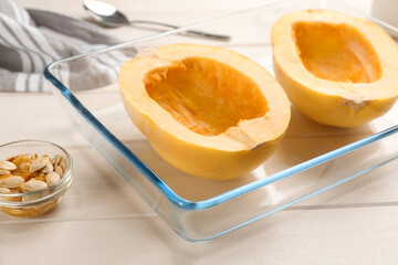 Halves of fresh spaghetti squash in baking dish on white wooden table, closeup. Cooking at home
