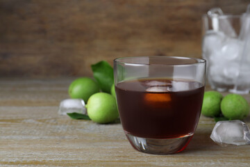 Delicious liqueur with ice and green walnuts on wooden table. Space for text