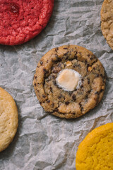 S'mores chocolate chip cookies on baking parchment surrounded by colored cookies.  Flatlay. 