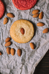 Small almond cookie surrounded by almonds and red cookies on baking parchment and wooden table