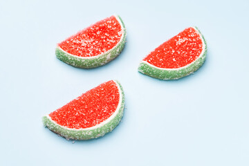 Jelly candies. Three watermelon jelly candies sprinkled with sugar on a blue background. Watermelon marmalade. Selective soft focus.