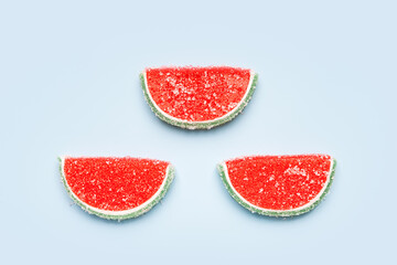 Jelly candies. Top view of three watermelon jelly candies sprinkled with sugar on a blue background. Watermelon marmalade. Selective soft focus.