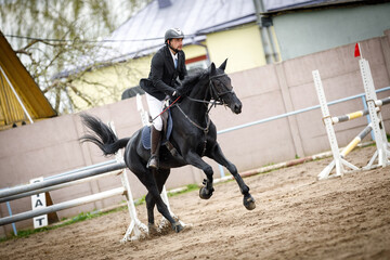portrait of black mare horse and adult man rider jumping during equestrian showjumping competition...