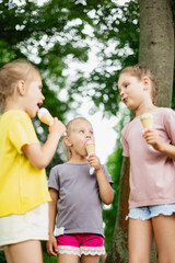 Low angle view of three girls eating ice cream and talking on hot summer day. Siblings walking outside and enjoying ice cream