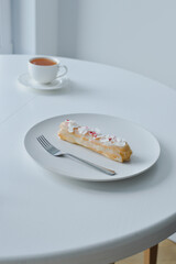 Eclair on white plate and fork and cup of tea - copy space and minimalistic