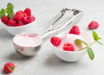 A scoop of homemade raspberry ice cream with fresh raspberries and mint in a white cup on a light background. Delicious and romantic dessert.